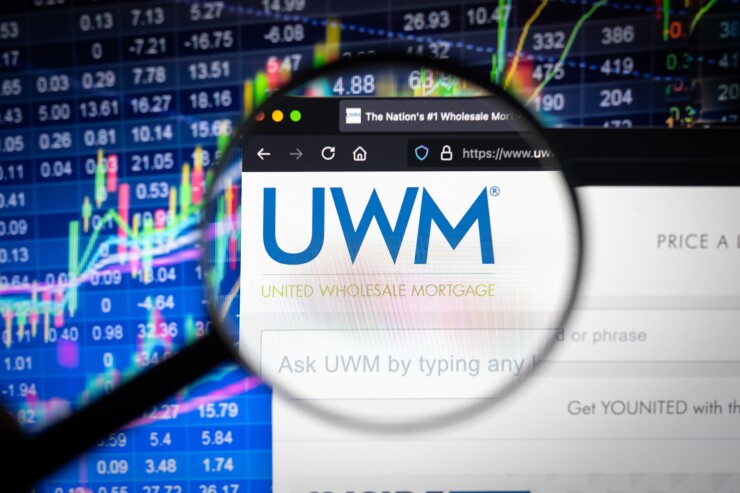 UWM United Wholesale Mortgage company logo on a website with blurry stock market developments in the background, seen on a computer screen through a magnifying glass